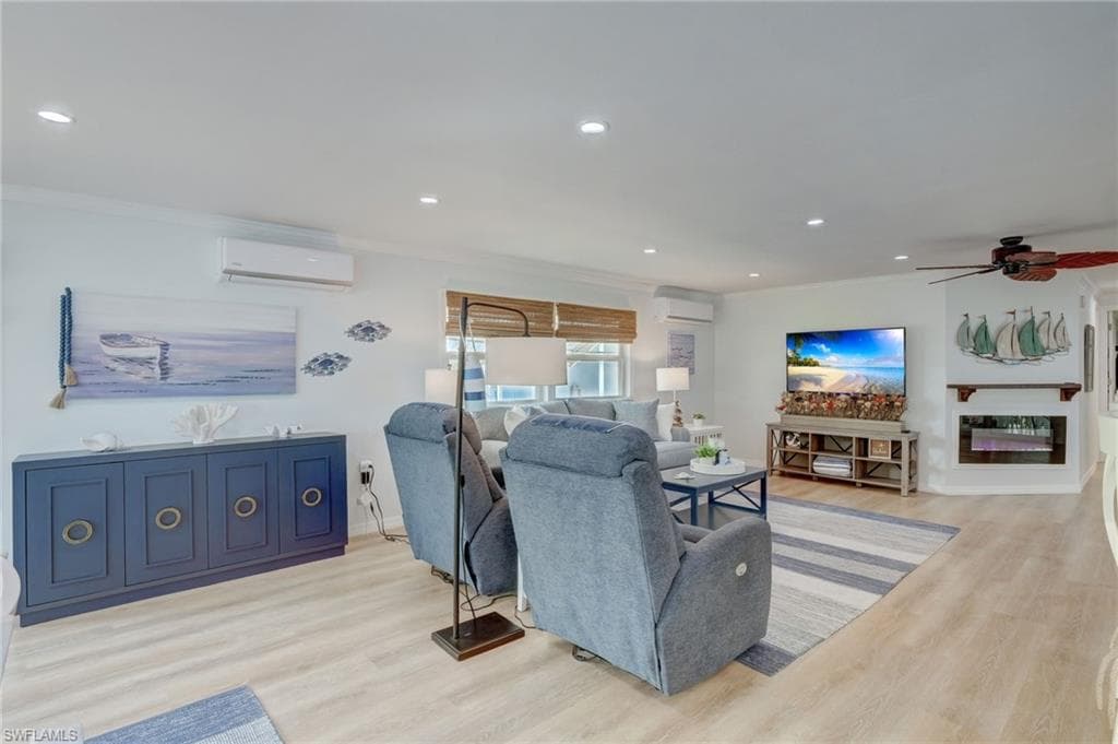 Living area with light wood-style flooring, recessed lighting, ornamental molding, ceiling fan, and a glass covered fireplace