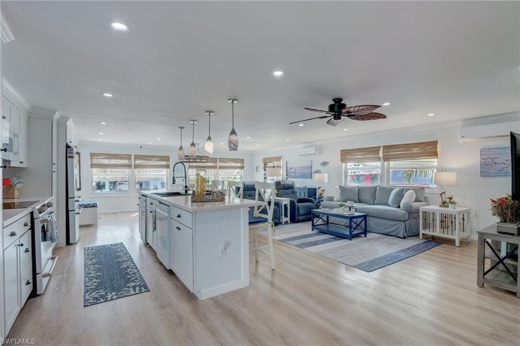 Kitchen with white cabinetry, white appliances, open floor plan, a kitchen island with sink, and light wood finished floors