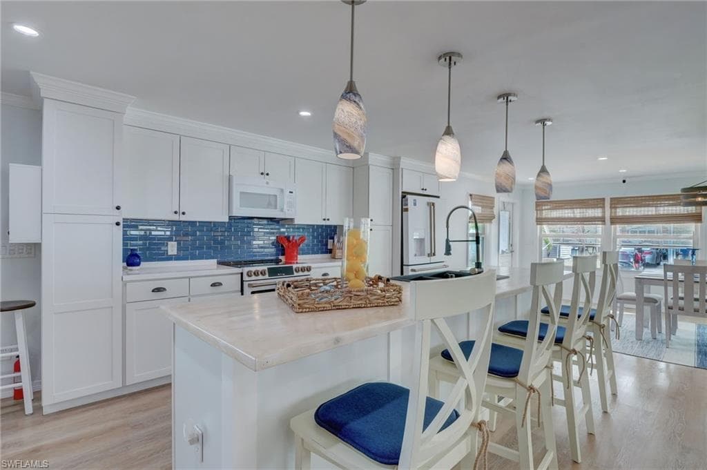 Kitchen featuring a breakfast bar, crown molding, light wood-style floors, an island with sink, and white cabinetry