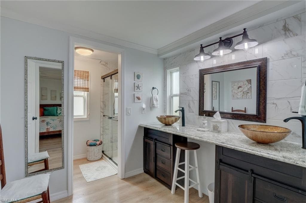 Full bath with crown molding, plenty of natural light, double vanity, a marble finish shower, and light wood finished floors