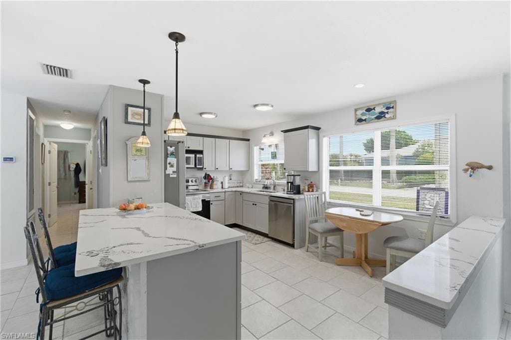 Kitchen with a center island, gray cabinets, light stone counters, stainless steel appliances, and a breakfast bar