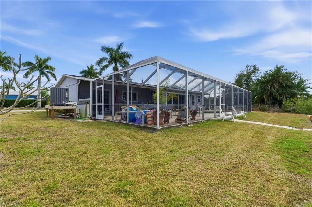 Back of house with glass enclosure, a sunroom, and a yard