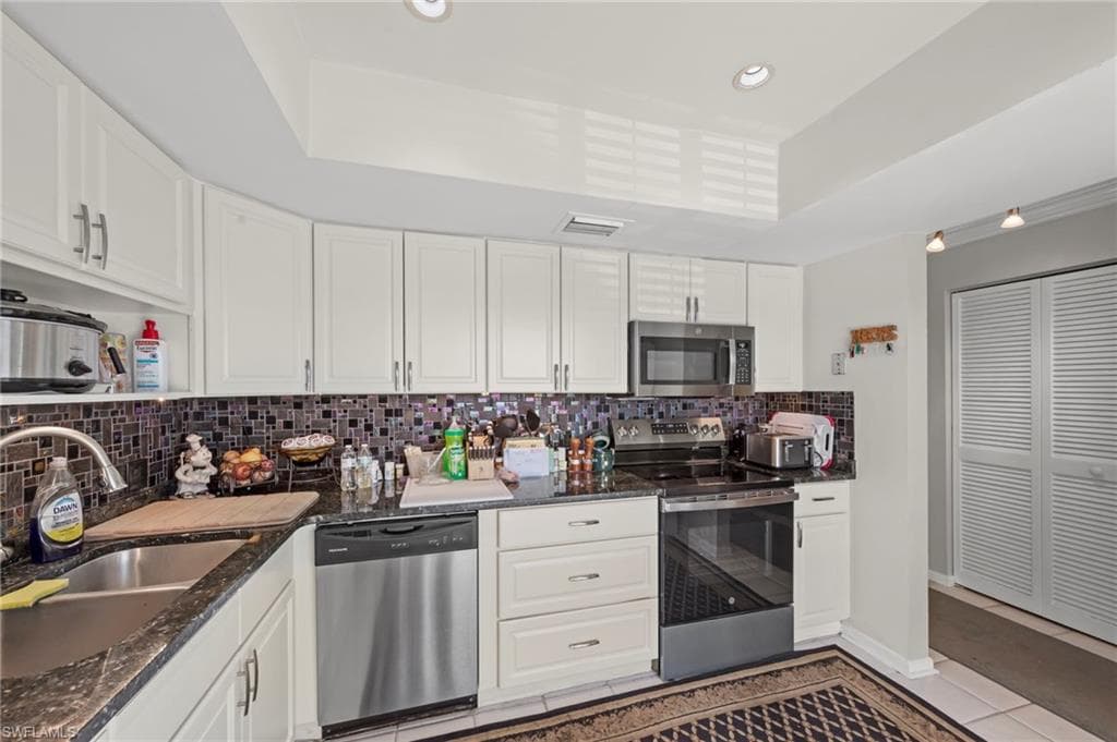 Kitchen featuring stainless steel appliances, white cabinets, dark stone counters, recessed lighting, and tasteful backsplash