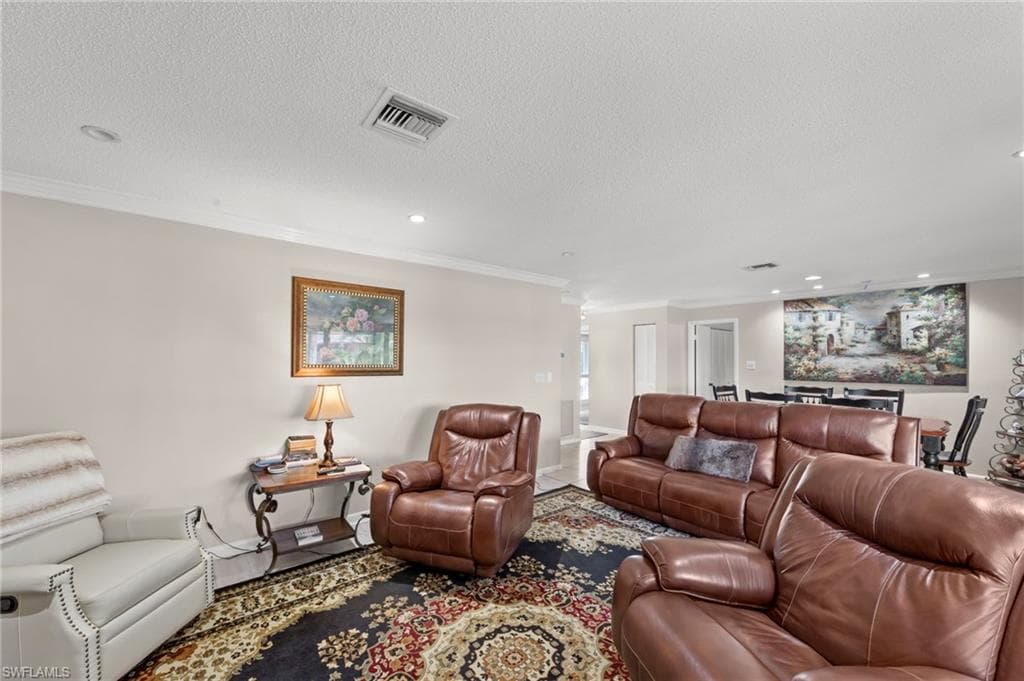 Living room with ornamental molding, recessed lighting, and a textured ceiling