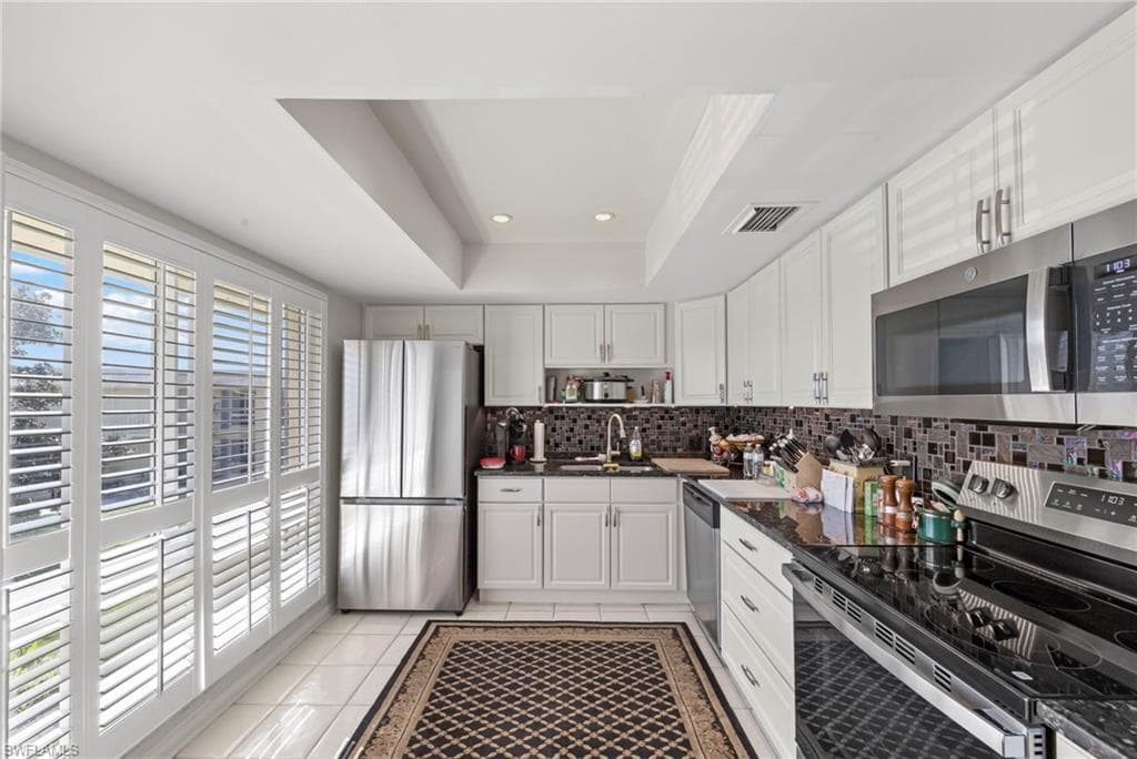 Kitchen with stainless steel appliances, white cabinetry, recessed lighting, a tray ceiling, and light tile patterned floors