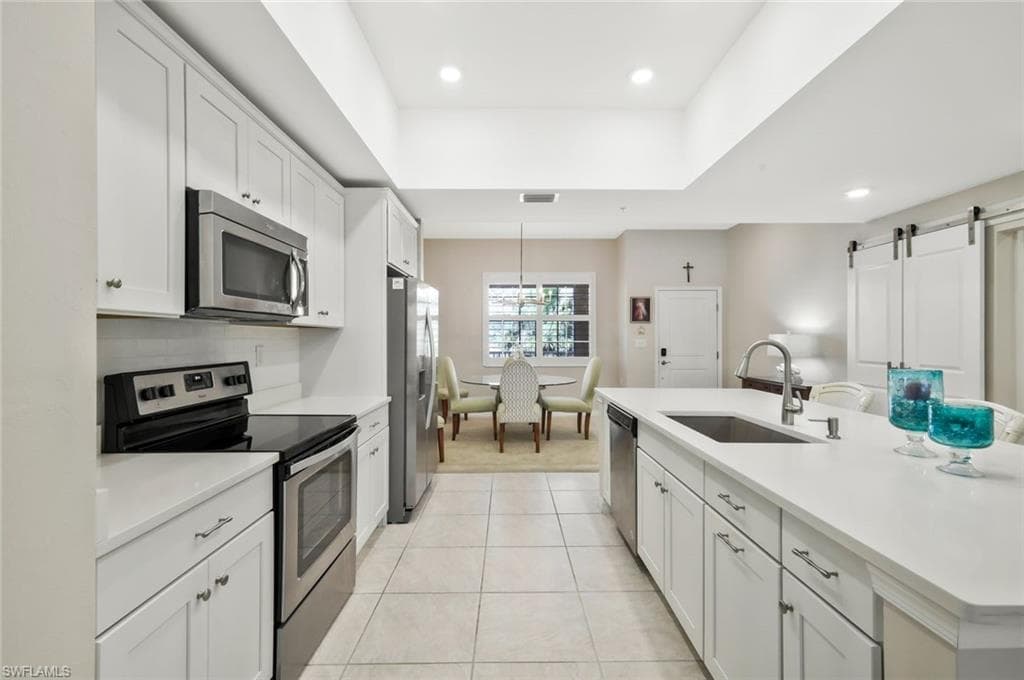 Kitchen with stainless steel appliances, white cabinetry, a barn door, a center island with sink, and backsplash