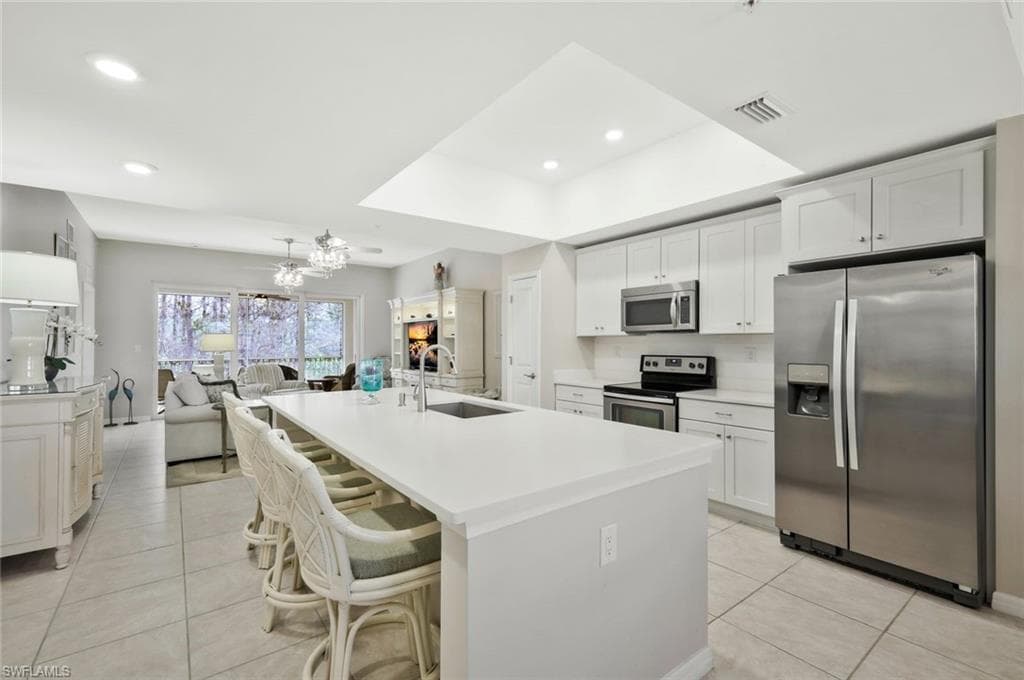 Kitchen with stainless steel appliances, a kitchen bar, white cabinets, a kitchen island with sink, and light tile patterned floors