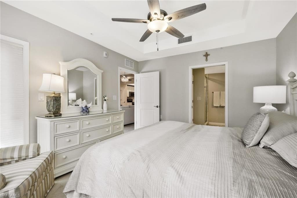 Carpeted bedroom with a ceiling fan, a raised ceiling, and ensuite bath