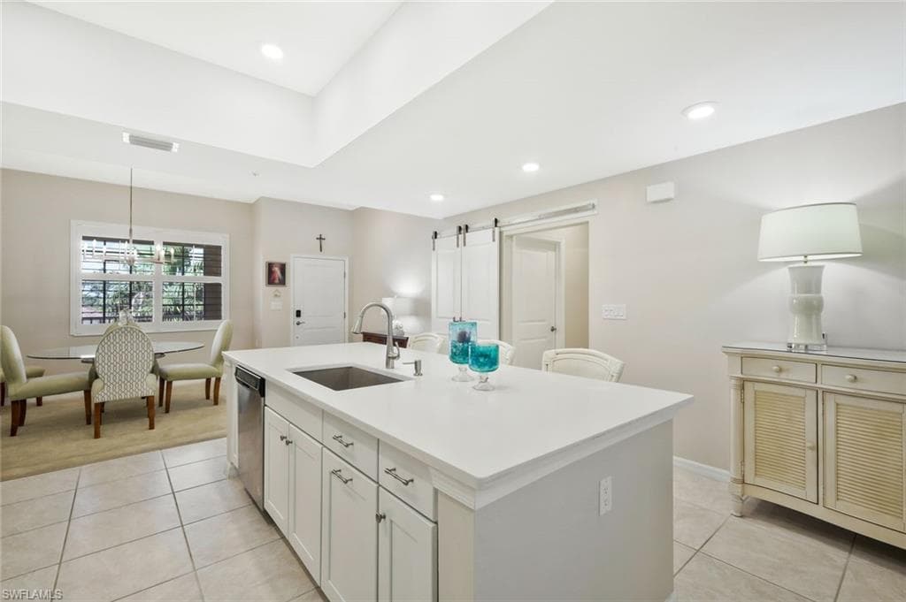 Kitchen featuring a barn door, a center island with sink, light tile patterned flooring, and white cabinetry