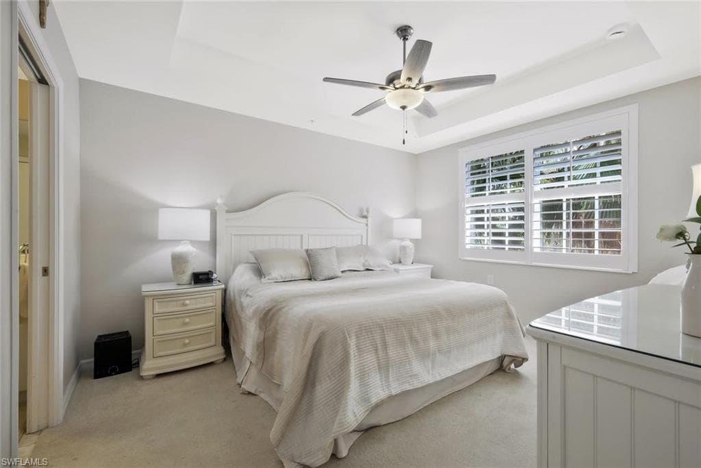 Bedroom with ceiling fan, a tray ceiling, and light colored carpet