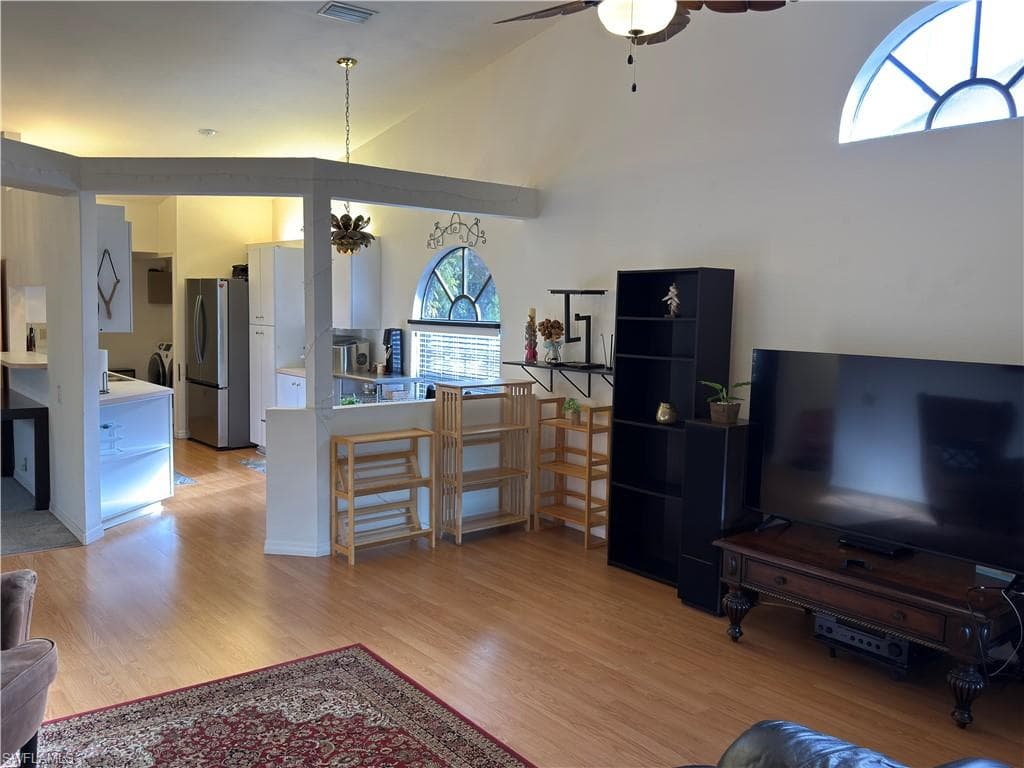 Living room with hanging lights, light wood-style flooring, a ceiling fan, and vaulted ceiling
