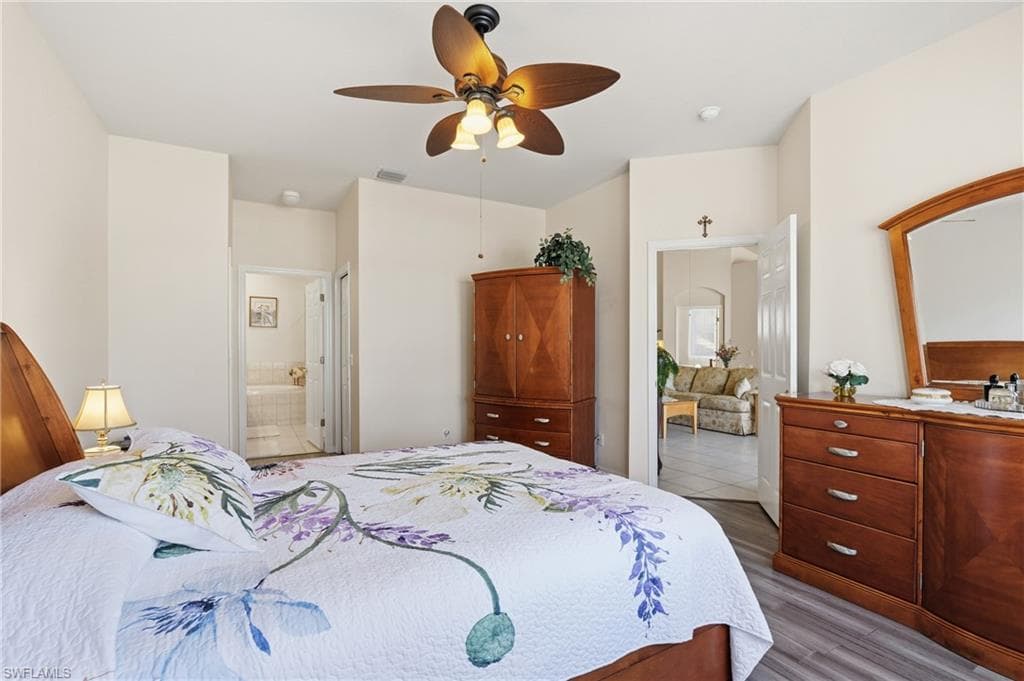 Bedroom with ensuite bathroom, ceiling fan, and wood finished floors
