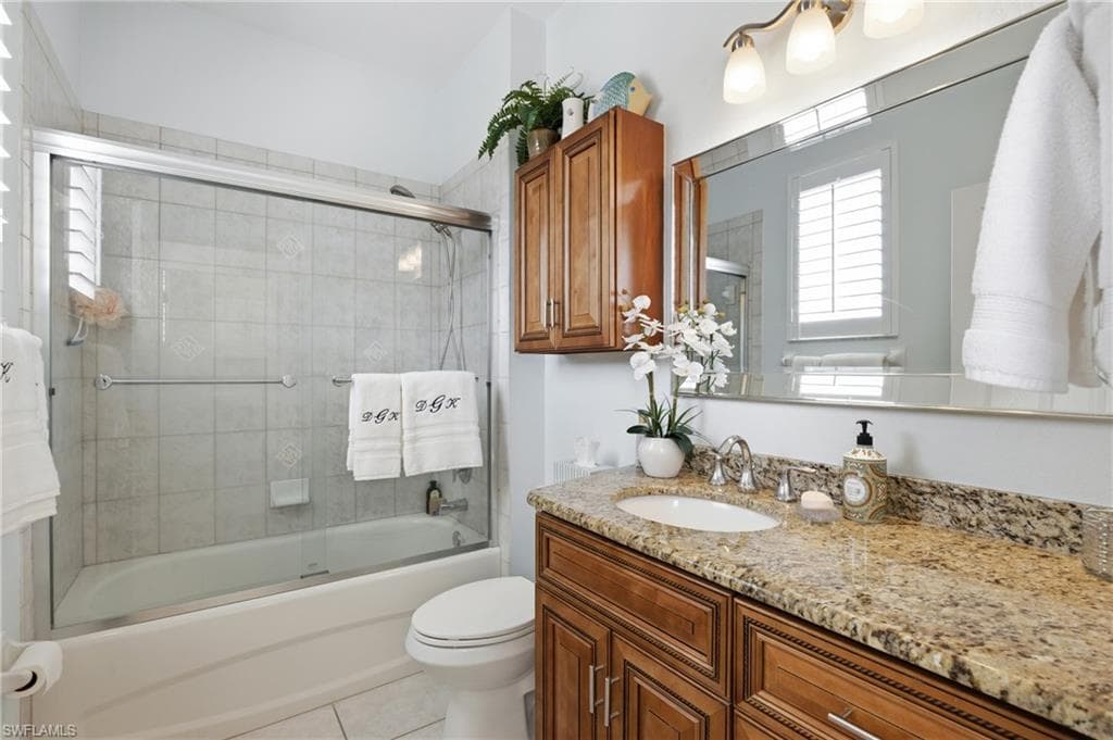 Full bath with vanity, bath / shower combo with glass door, and light tile patterned flooring