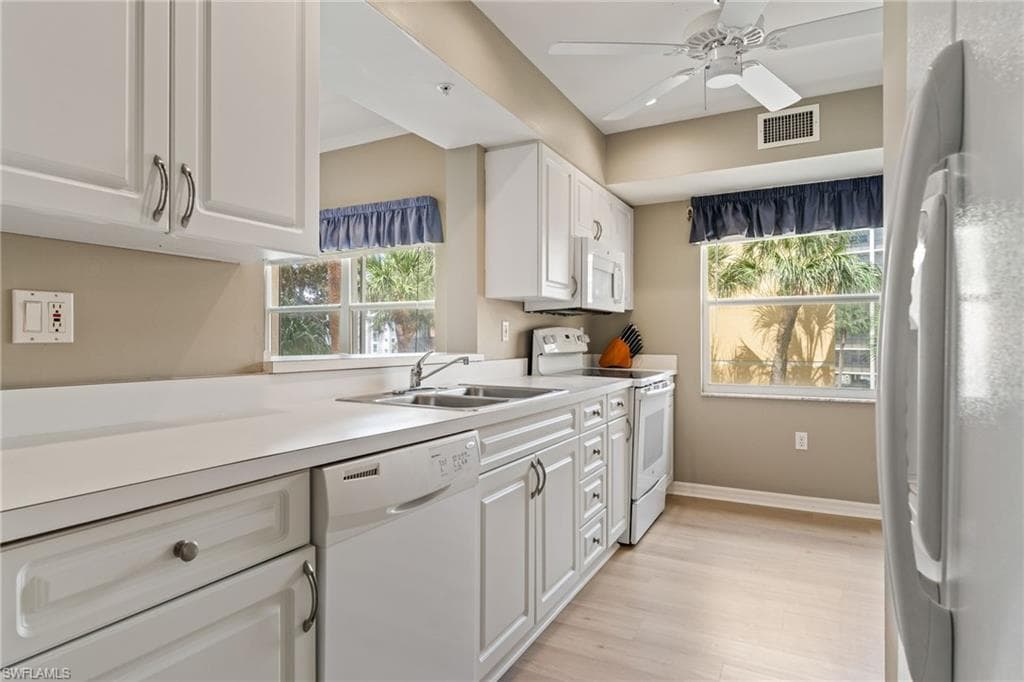 Kitchen featuring white appliances, white cabinetry, light countertops, ceiling fan, and light wood-type flooring