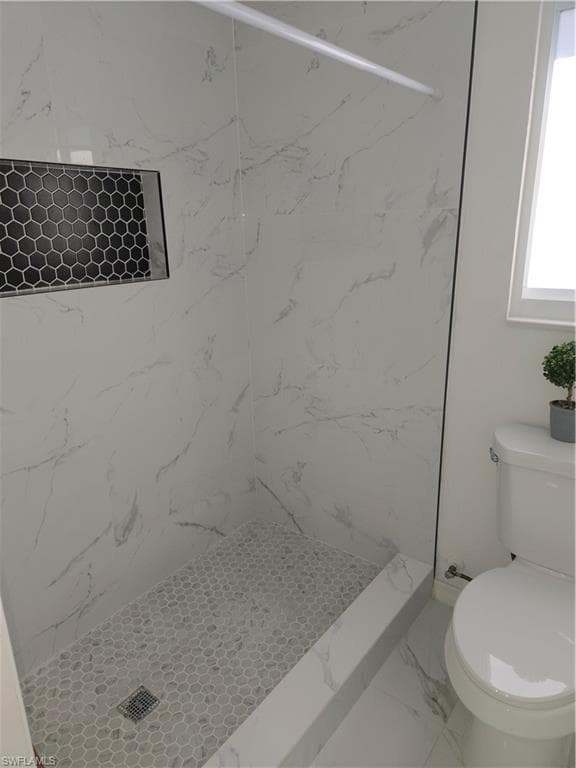 Full bath featuring a marble finish shower and marble look tile flooring