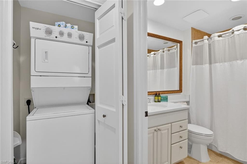 Full bathroom featuring vanity, a shower with shower curtain, stacked washer and dryer, and light tile patterned flooring
