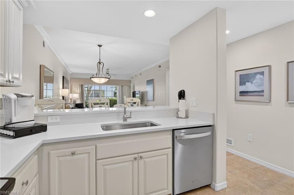 Kitchen featuring dishwasher, white cabinets, decorative light fixtures, light stone countertops, and crown molding