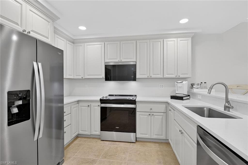 Kitchen with stainless steel appliances, white cabinets, light stone counters, and recessed lighting