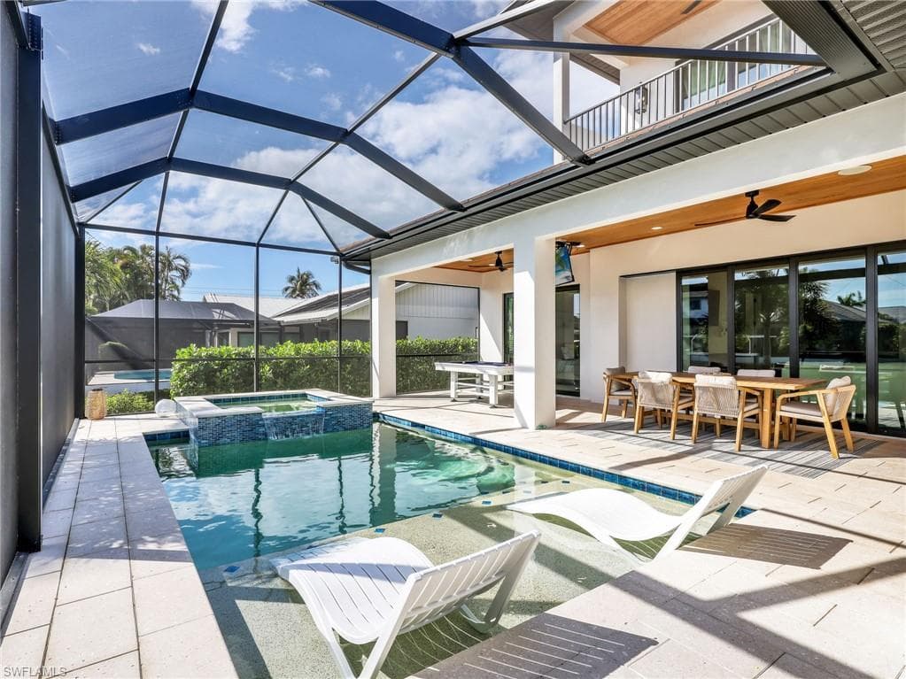 Combined pool / hot tub featuring outdoor dining area, a sunroom, a patio, and glass enclosure