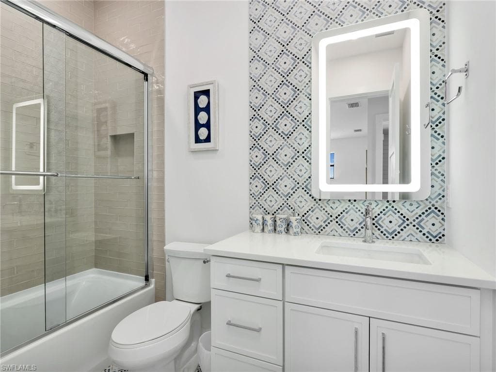 Bathroom featuring vanity, bath / shower combo with glass door, and backsplash
