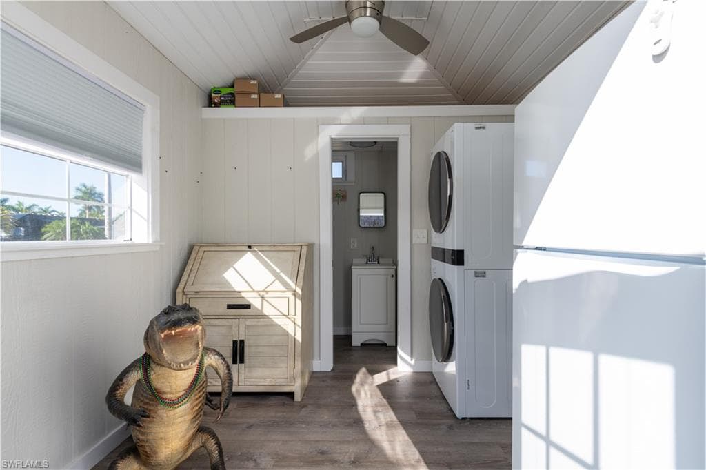 Laundry area featuring a ceiling fan, stacked washer and dryer, dark wood-type flooring, and wood ceiling