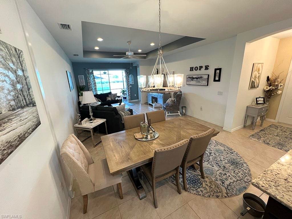 Dining room with a raised ceiling, light tile patterned floors, ceiling fan, and a chandelier