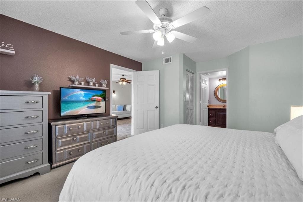 Bedroom with a textured ceiling, light colored carpet, ceiling fan, a closet, and ensuite bathroom