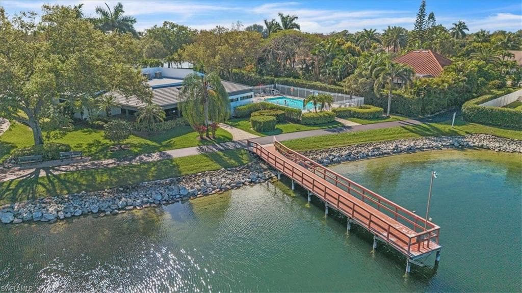 Dock area with a lawn, a water view, a pool, and view of wooded area
