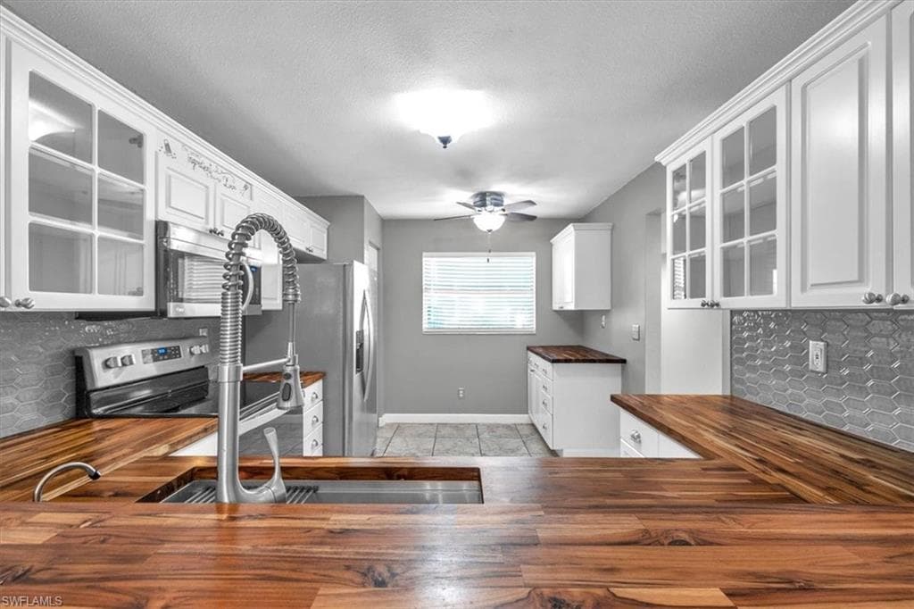 Kitchen featuring glass insert cabinets, backsplash, stainless steel appliances, white cabinetry, and wooden counters