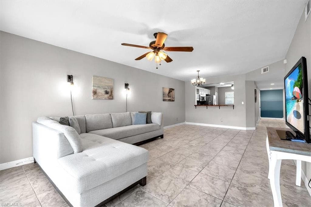 Living room with a ceiling fan, suspended lighting, and light marble finish floors
