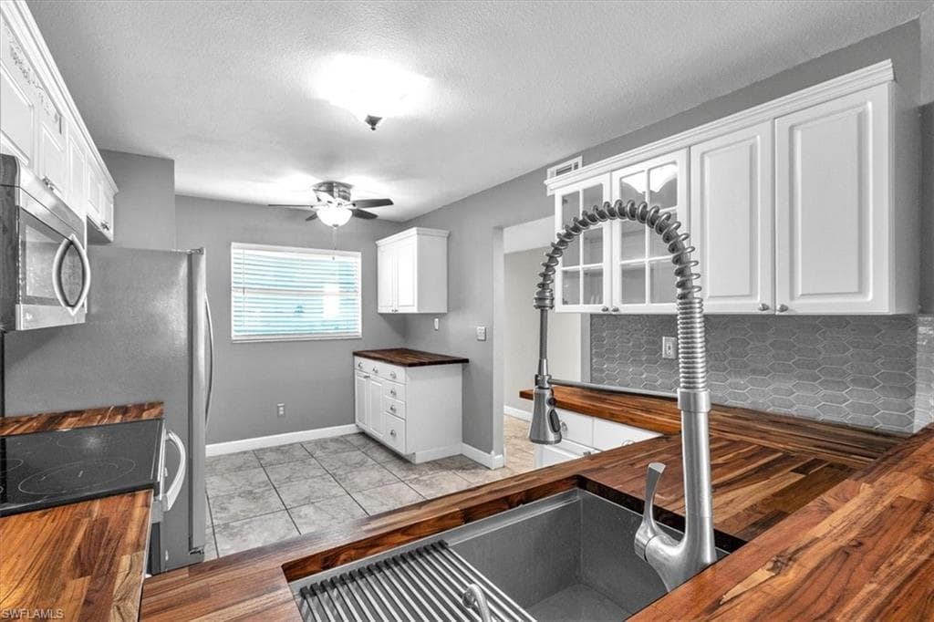 Kitchen with wood counters, stainless steel microwave, white cabinets, range with electric stovetop, and light wood-style floors