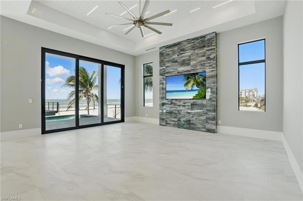Unfurnished living room featuring a wooden tray ceiling, plenty of natural light, ceiling fan, and light marble finish flooring Virtually Enhanced