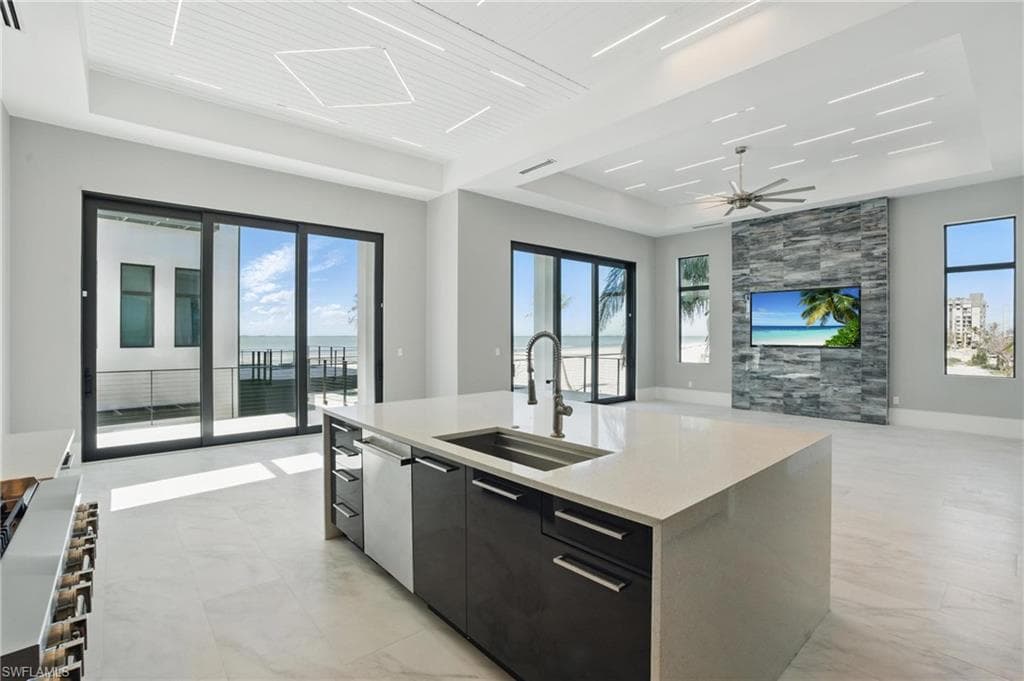 Kitchen featuring an island with sink, dark cabinetry, open floor plan, a tray ceiling, and modern cabinets Virtually Enhanced