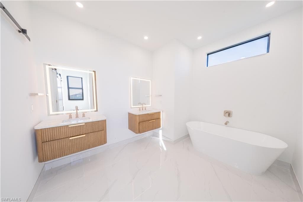 Bathroom with two vanities, recessed lighting, a soaking tub, and light marble finish floors