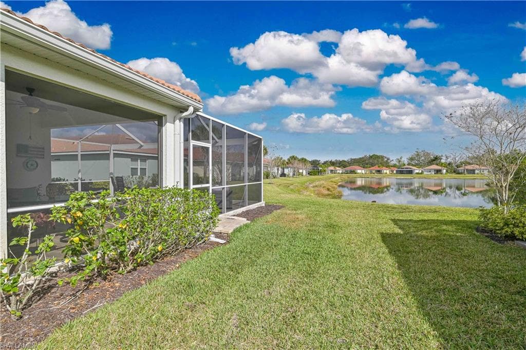 View of grassy yard featuring a lanai, a water view, a residential view, and a sunroom