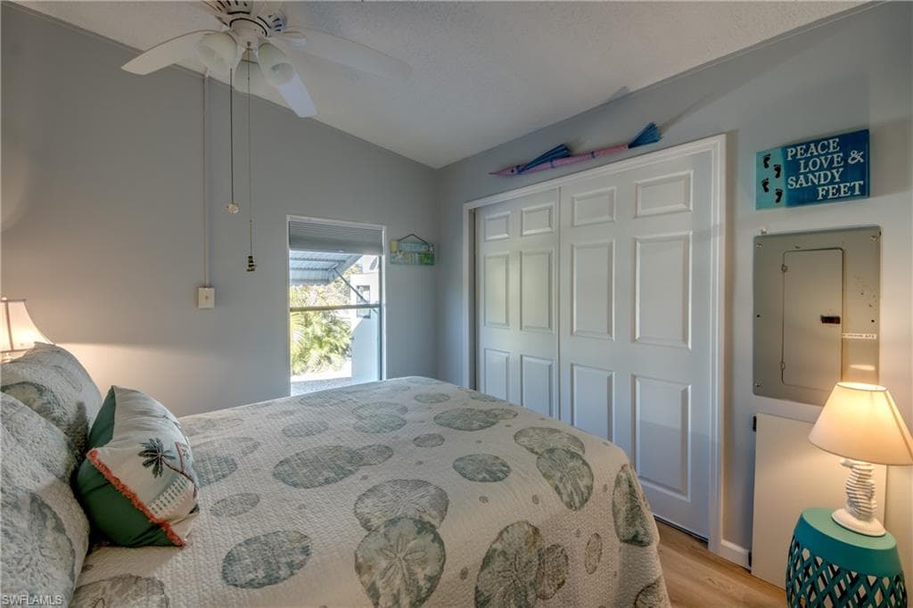 Bedroom with electric panel, light wood-type flooring, a closet, vaulted ceiling, and ceiling fan