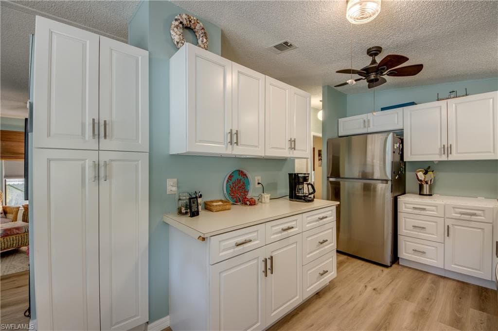 There is a new counter top installed after pictures were taken. Kitchen featuring a ceiling fan, freestanding refrigerator, light wood-type flooring, light countertops, and white cabinets