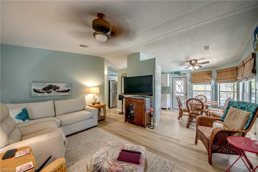 Living room with a ceiling fan, a textured ceiling, and light wood-style floors