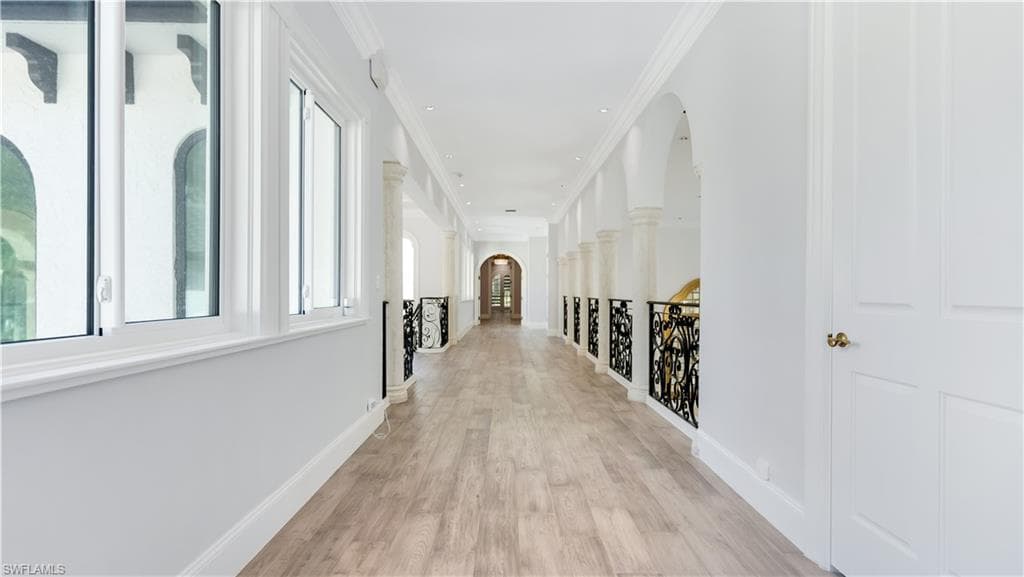 Hallway with arched walkways, light wood-style flooring, ornamental molding, and an upstairs landing