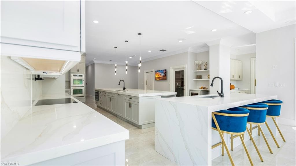 Kitchen featuring light stone counters, a kitchen bar, crown molding, stainless steel double oven, and decorative light fixtures