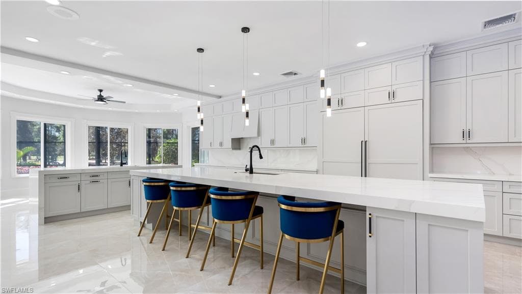 Kitchen with a spacious island, a breakfast bar area, a ceiling fan, and light stone countertops