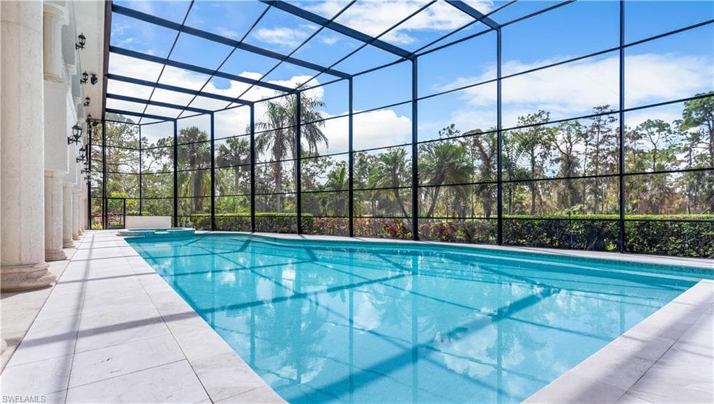 Combined pool / hot tub with glass enclosure, a sunroom, and a patio