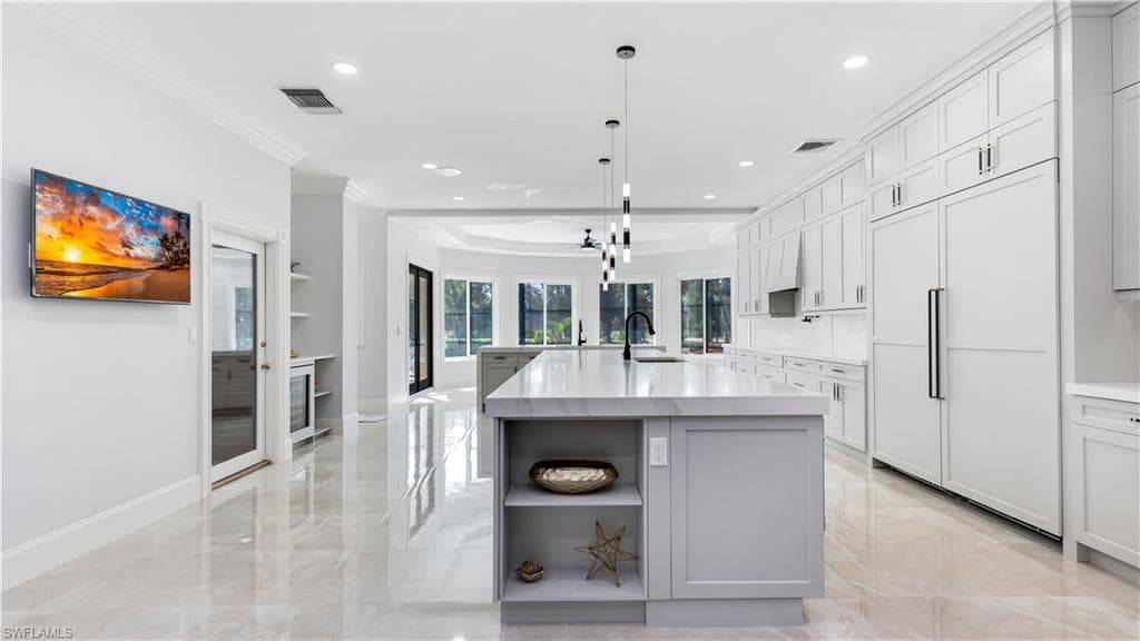 Kitchen with open shelves, a large island, paneled fridge, ornamental molding, and light stone countertops