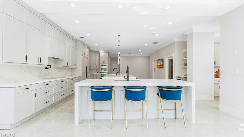 Kitchen featuring light stone counters, a breakfast bar area, crown molding, decorative backsplash, and hanging light fixtures