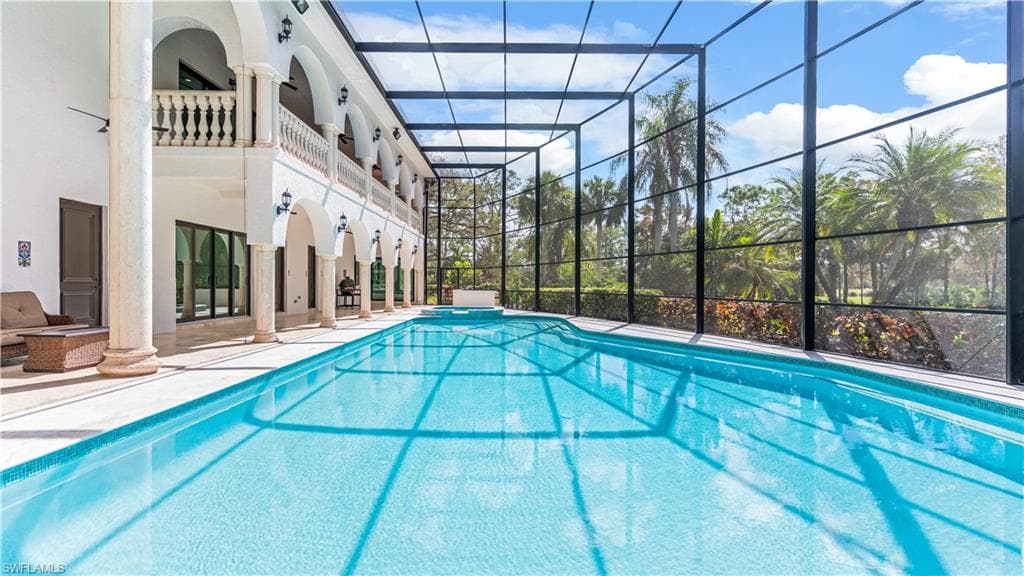 Combined pool / hot tub with glass enclosure, a patio area, and a balcony