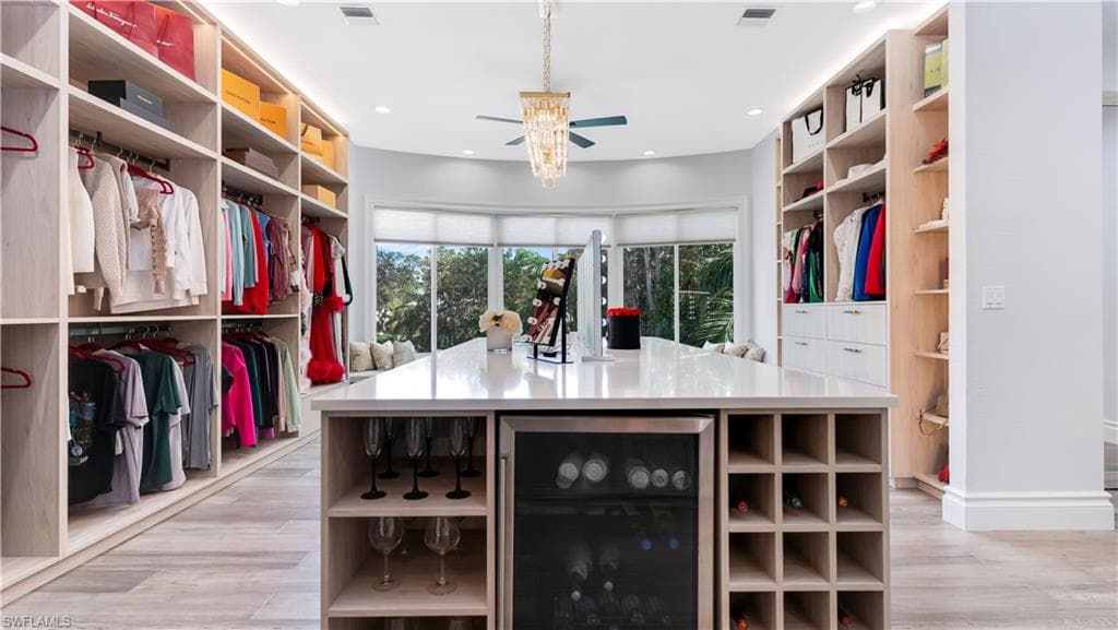Walk in master closet with wine cooler, a ceiling fan, and light wood-type flooring