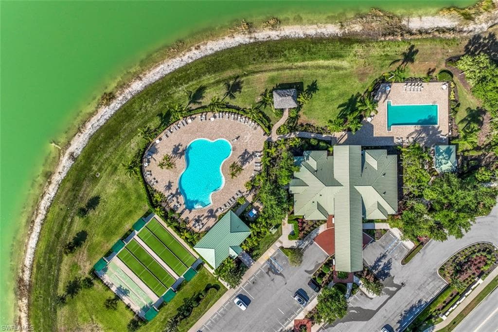 Aerial view featuring a lakeside setting, a resort-style pool with lounge seating, an additional rectangular swimming pool, and a building with a multi-gabled roof