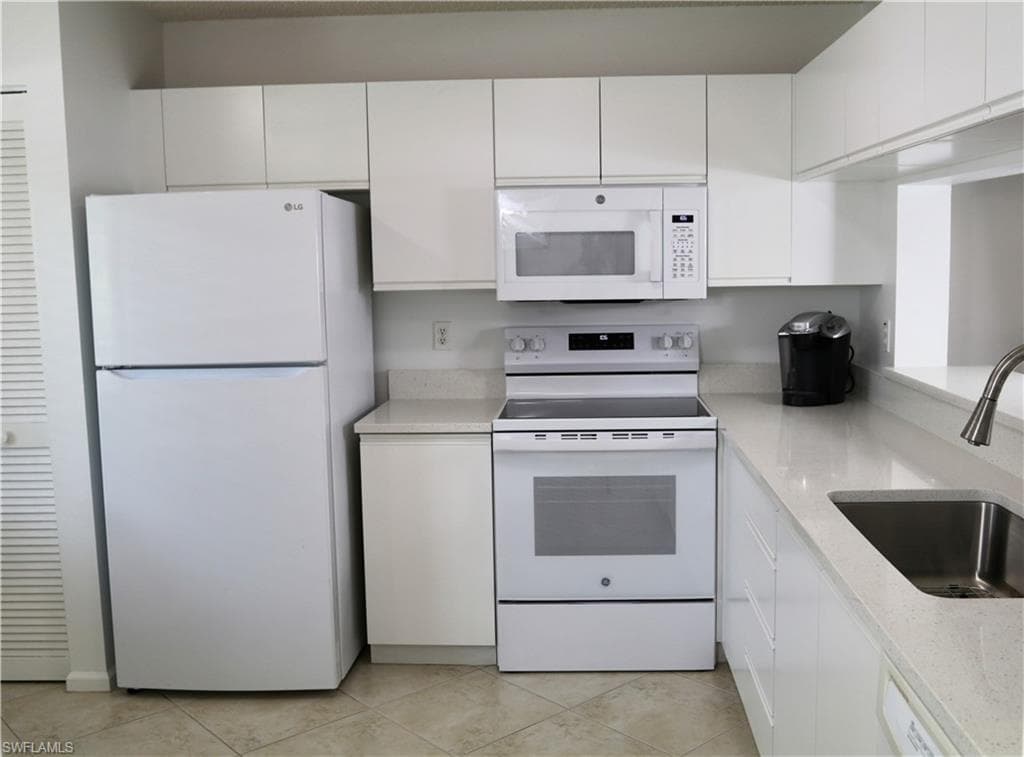 Kitchen with white appliances, white cabinets, and light stone countertops