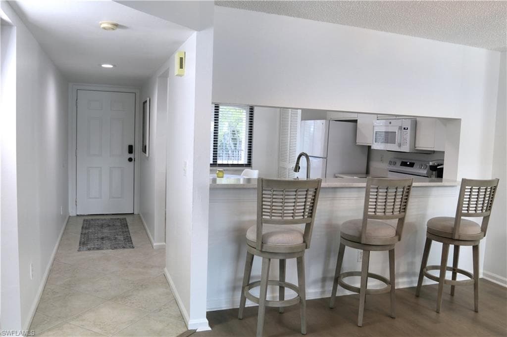 Kitchen featuring white appliances, a peninsula, white cabinets, a breakfast bar area, and recessed lighting
