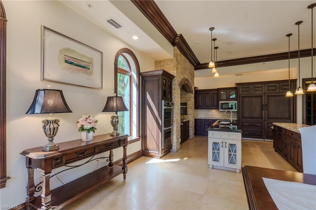 Two tone kitchen featuring dual tone cabinetry, crown molding, dark stone countertops, tasteful backsplash, and hanging light fixtures